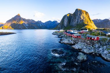 Norveç 'in Hamnoy, Lofoten Adaları' nda gün doğumu, kıyı şeridi boyunca geleneksel kırmızı evler ve dramatik dağlar..