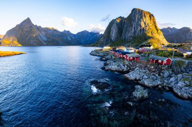 Sunrise over Hamnoy, Lofoten Islands, Norway, with traditional red houses and dramatic mountains along the coastline. clipart