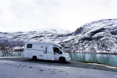 A motorhome driving along the Sognefjellsvegen road in south Norway, surrounded by snow-covered mountains and scenic views. clipart