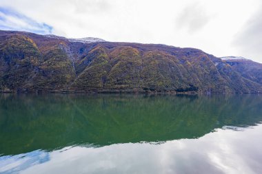 Norveç 'in Lustrafjorden kentindeki sonbahar manzarasında berrak su yansımaları, dağlar ve renkli yeşillikler yer almaktadır..