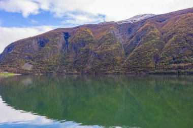Norveç 'in Lustrafjorden kentindeki sonbahar manzarasında berrak su yansımaları, dağlar ve renkli yeşillikler yer almaktadır..