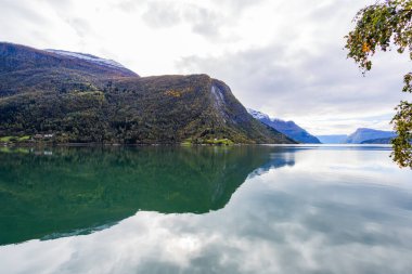 Norveç 'in Lustrafjorden kentindeki sonbahar manzarasında berrak su yansımaları, dağlar ve renkli yeşillikler yer almaktadır..