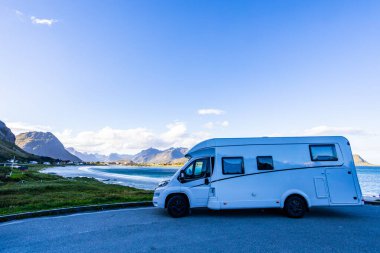 A motorhome parked by the scenic coast of Lofoten Islands in Norway, surrounded by mountains and clear skies. clipart