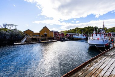 Norveç, Lofoten Adaları 'ndaki Nusfjord manzaralı, kırmızı ve sarı ahşap evler, tekneler ve kristal berrak sularla.