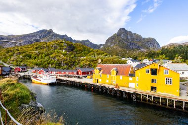Norveç, Lofoten Adaları 'ndaki Nusfjord manzaralı, kırmızı ve sarı ahşap evler, tekneler ve kristal berrak sularla.