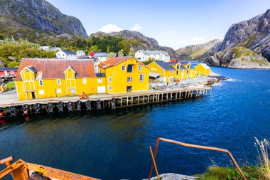 Norveç, Lofoten Adaları 'ndaki Nusfjord manzaralı, kırmızı ve sarı ahşap evler, tekneler ve kristal berrak sularla.