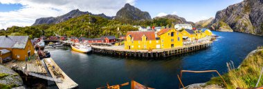 Norveç, Lofoten Adaları 'ndaki Nusfjord manzaralı, kırmızı ve sarı ahşap evler, tekneler ve kristal berrak sularla.