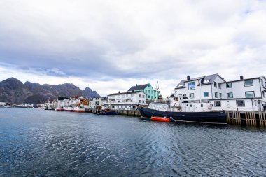 Norveç, Lofoten Adaları 'ndaki Henningsvaer manzarası liman boyunca uzanan ve arka planda dağlar bulunan geleneksel binaları gösteriyor..