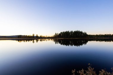 İsveç 'in kuzeyindeki Laponya gölünde sakin bir günbatımı. Durgun sularda ağaçların yansıması..