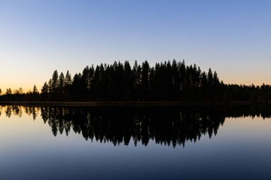 İsveç 'in kuzeyindeki Laponya gölünde sakin bir günbatımı. Durgun sularda ağaçların yansıması..