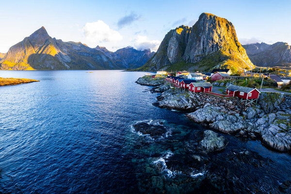 Sunrise over Hamnoy, Lofoten Islands, Norway, with traditional red houses and dramatic mountains along the coastline.