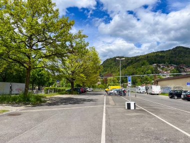 Thun, İsviçre; 5 Mayıs 2024: Kamp araçları ve gür ağaçlarla dolu manzaralı park yeri açık, güneşli bir günde mavi gökyüzü altında tüylü bulutlar