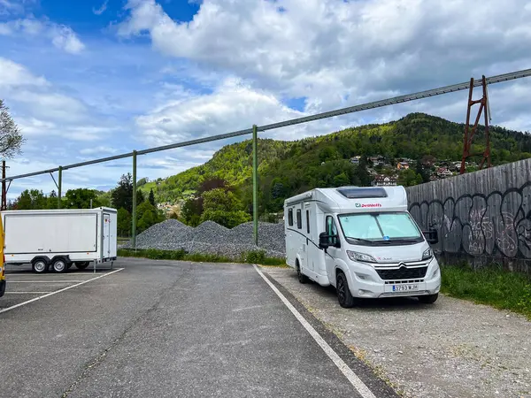 Thun, İsviçre; 5 Mayıs 2024: Otoparka park etmiş beyaz bir karavan ve arka planda bir treyleri olan yeşil bir tepe.