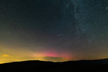 Aurora borealis gece gökyüzünü parlak renklerle aydınlatıyor, Coll De La Creueta, Pyrenees, Barselona, İspanya 'daki sayısız yıldızın ardından kayan yıldızlar. Ağustos 2024