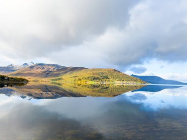 Norveç, Senja Adası 'nın sonbahar manzarası. Renkli ağaçlar, dingin su yansımaları ve dramatik dağlar..