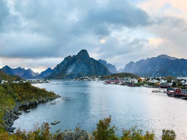 Autumn sunset in Reine, Lofoten Islands, northern Norway, with dramatic mountains, calm waters, and traditional houses along the shore. clipart