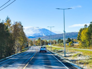 Güzel manzaralı bir güzergah, parlak sonbahar manzarası boyunca kar kaplı görkemli bir dağ zirvesine doğru ilerlerken berrak mavi gökyüzünün zeminine karşı.