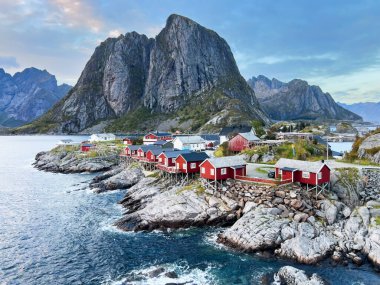 Norveç 'in Hamnoy, Lofoten Adaları' nda gün doğumu, kıyı şeridi boyunca geleneksel kırmızı evler ve dramatik dağlar..