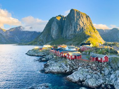 Norveç 'in Hamnoy, Lofoten Adaları' nda gün doğumu, kıyı şeridi boyunca geleneksel kırmızı evler ve dramatik dağlar..