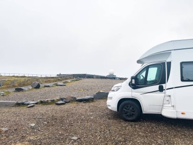 Sisli bir günde iki karavan manzaralı bir yere park edilmiş, doğanın sakinliği ve enginliğinin tadını çıkarıyorlar. Nordkapp