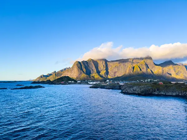 Norveç 'in Hamnoy, Lofoten Adaları' nda gün doğumu, kıyı şeridi boyunca geleneksel kırmızı evler ve dramatik dağlar..