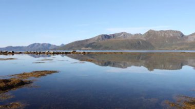 Sakin su, Norveç 'in kuzeyindeki açık bir günde, uzaktaki dağların yansımasını yaratır.