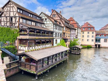 Strasbourg, Fransa; 7 Mayıs 2024: Strasbourg, Fransa 'da bahar mevsimi, parlak bir gökyüzüne sahip güzel bir nehir boyunca yarım ahşap binalar sergiliyor. 4K UHD