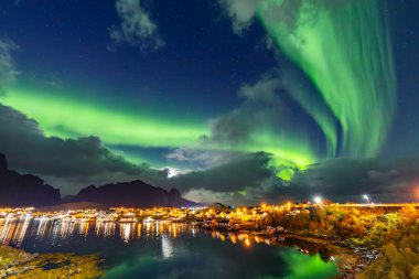 Kuzey Işıkları Reine üzerinde, Lofoten Adaları, Kuzey Norveç, gökyüzünü şehrin üzerinde canlı renklerle aydınlatıyor..