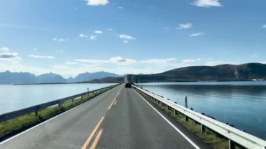 Araçlar Norveç 'in Lofoten adalarında dağları olan manzaralı bir sahil yolunda köprüye yaklaşıyorlar.