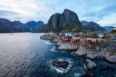 Norveç 'in Hamnoy, Lofoten Adaları' nda gün doğumu, kıyı şeridi boyunca geleneksel kırmızı evler ve dramatik dağlar..