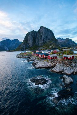 Norveç 'in Hamnoy, Lofoten Adaları' nda gün doğumu, kıyı şeridi boyunca geleneksel kırmızı evler ve dramatik dağlar..