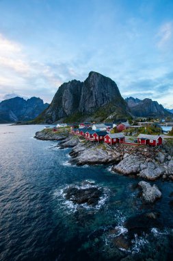 Norveç 'in Hamnoy, Lofoten Adaları' nda gün doğumu, kıyı şeridi boyunca geleneksel kırmızı evler ve dramatik dağlar..