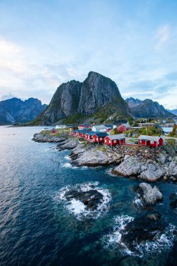 Norveç 'in Hamnoy, Lofoten Adaları' nda gün doğumu, kıyı şeridi boyunca geleneksel kırmızı evler ve dramatik dağlar..