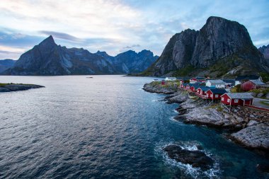 Norveç 'in Hamnoy, Lofoten Adaları' nda gün doğumu, kıyı şeridi boyunca geleneksel kırmızı evler ve dramatik dağlar..
