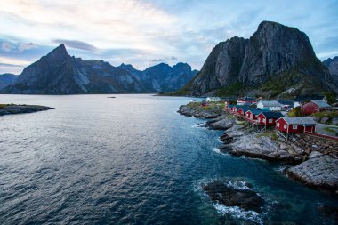 Norveç 'in Hamnoy, Lofoten Adaları' nda gün doğumu, kıyı şeridi boyunca geleneksel kırmızı evler ve dramatik dağlar..