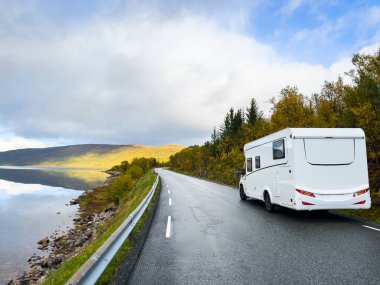 Motorhome and autumn landscape of Senja Island, Norway, with colorful trees, serene water reflections, and dramatic mountains. clipart