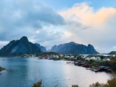 Norveç 'in kuzeyindeki Reine, Lofoten Adaları' nda sonbahar günbatımı, dramatik dağlar, sakin sular ve kıyı boyunca geleneksel evler..