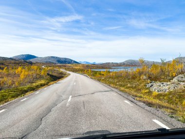 Motorhome driving on a scenic road in Kiruna, Sweden, with autumn foliage and beautiful lake. clipart