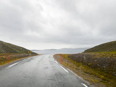 Norveç 'te bulutlu bir gökyüzünün altında nefes kesen manzaralı bir yol. Nordkapp