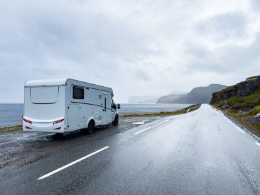 White camper van driving on e69 road to nordkapp, norway, in a rainy and foggy day clipart