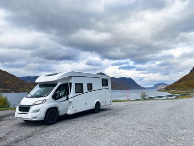 A motorhome parked by the road in the autumn landscape of the Lyngen Alps, Norway, with mountains. clipart