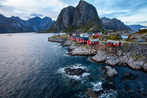 Norveç 'in Hamnoy, Lofoten Adaları' nda gün doğumu, kıyı şeridi boyunca geleneksel kırmızı evler ve dramatik dağlar..