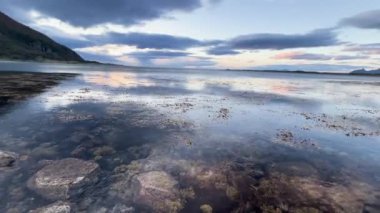 Su, Norveç 'in Lofoten adalarındaki bulutlu bir günbatımını ve dağları yansıtır.