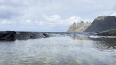 Okyanus dalgaları Norveç, Senja 'da dağları olan kayalık bir kıyıya çarpıyor.