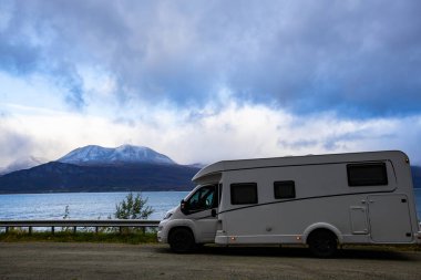 A motorhome parked by the road in the autumn landscape of the Lyngen Alps, Norway, with mountains. clipart