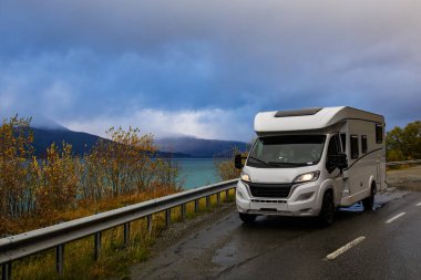 A motorhome parked by the road in the autumn landscape of the Lyngen Alps, Norway, with mountains. clipart