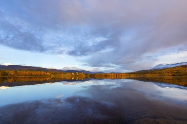 Norveç 'in sonbahar manzarası, renkli ağaçlar, dingin su yansımaları ve dramatik dağlar..