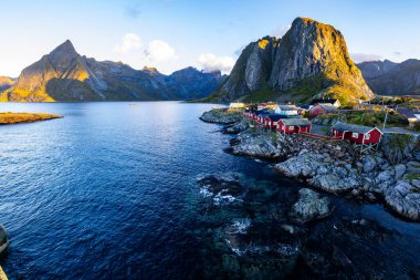 Norveç 'in Hamnoy, Lofoten Adaları' nda gün doğumu, kıyı şeridi boyunca geleneksel kırmızı evler ve dramatik dağlar..