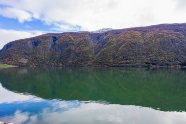 Norveç 'in Lustrafjorden kentindeki sonbahar manzarasında berrak su yansımaları, dağlar ve renkli yeşillikler yer almaktadır..