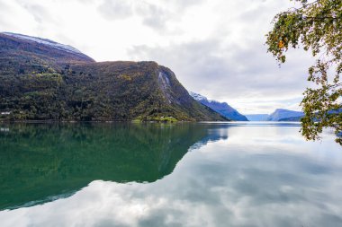 Norveç 'in Lustrafjorden kentindeki sonbahar manzarasında berrak su yansımaları, dağlar ve renkli yeşillikler yer almaktadır..